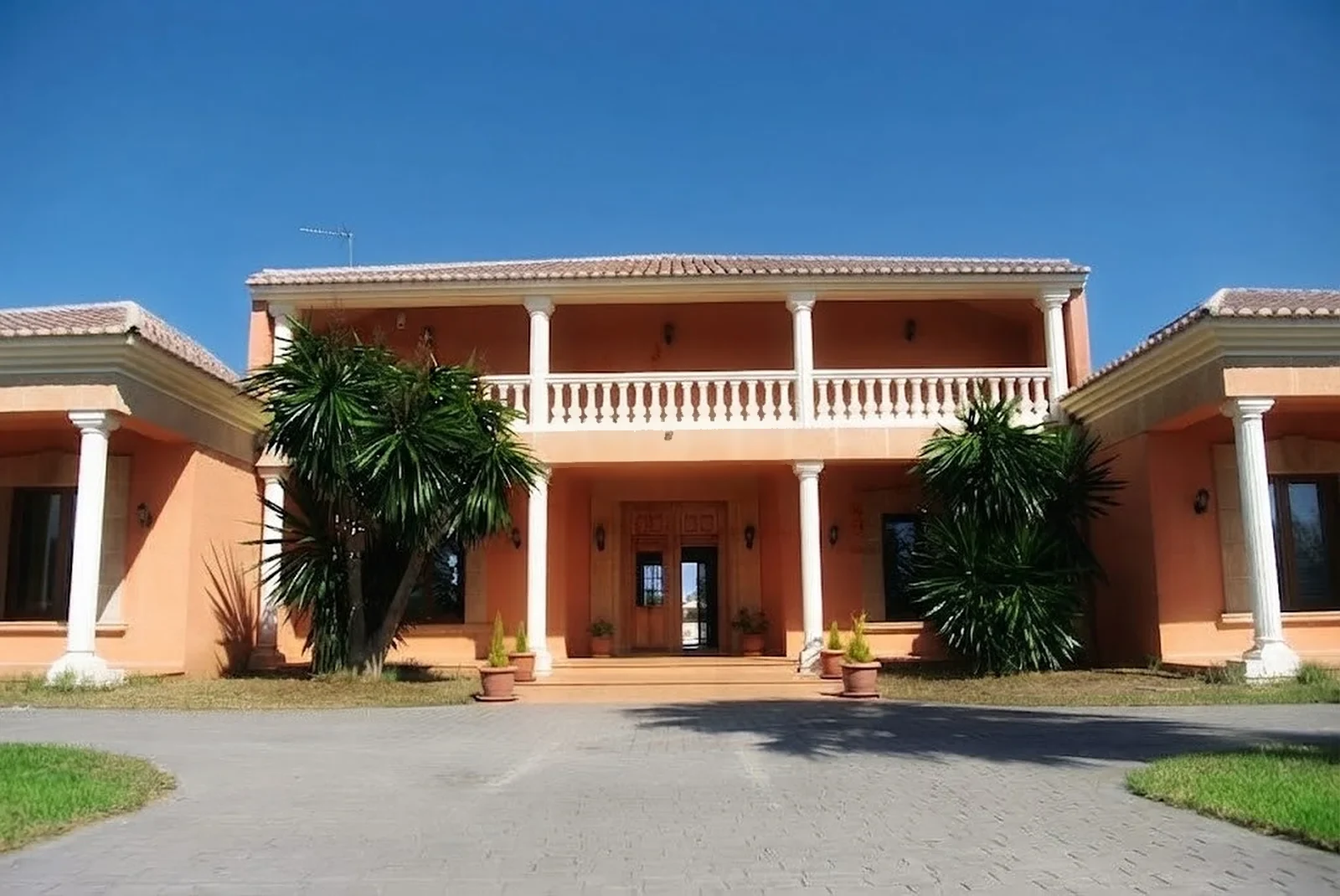 Fachada principal con balcón en la planta alta, columnas blancas y la puerta de entrada