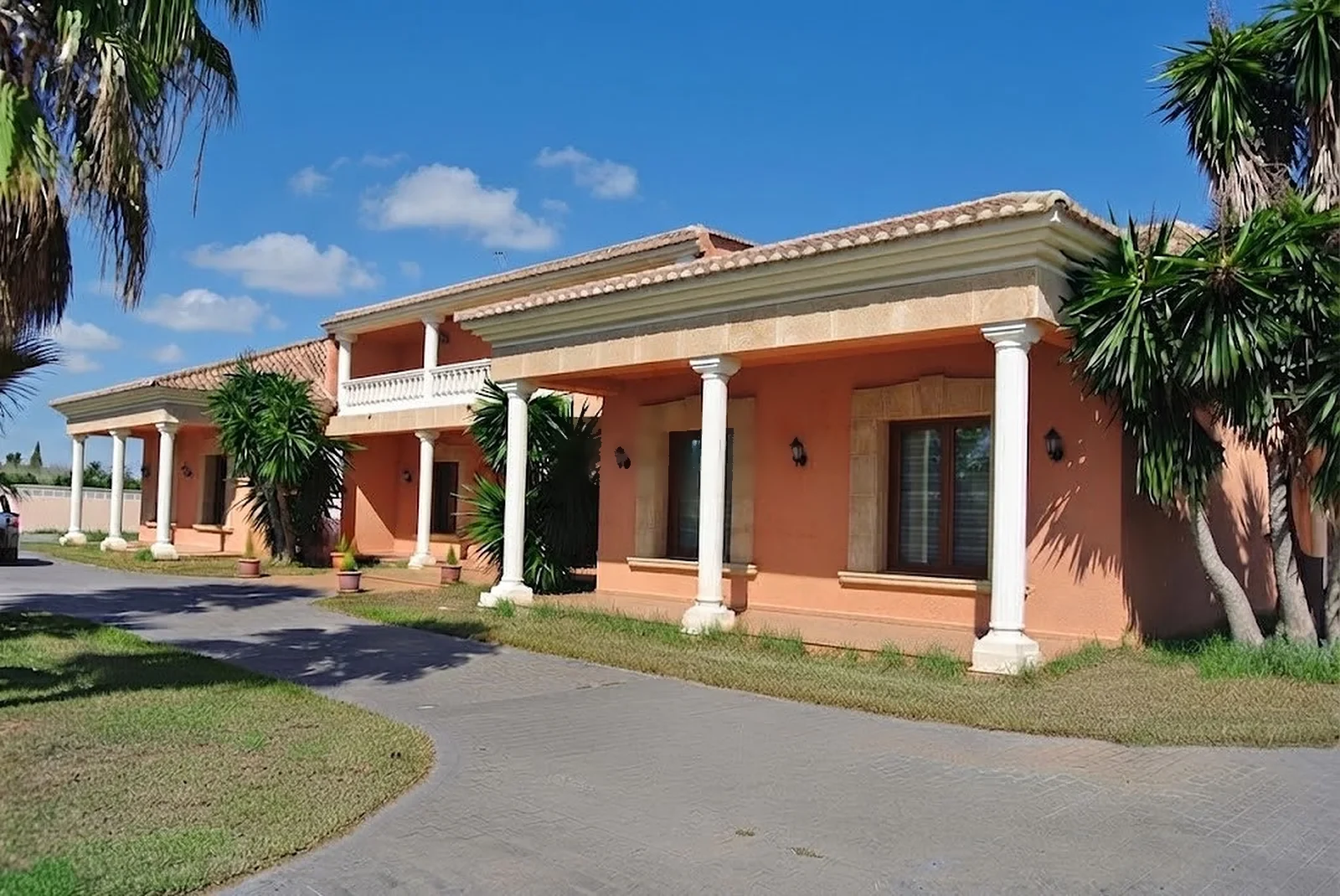 Lateral de la casa: terraza cubierta con columnas, muros de color salmón y palmeras